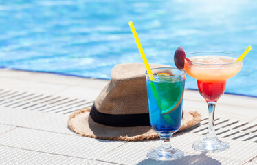 Two colorful cocktail glasses at the edge of swimming pool