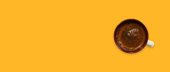 Brown cup of coffee on a warm yellow background. Banner with copy space. Top view
