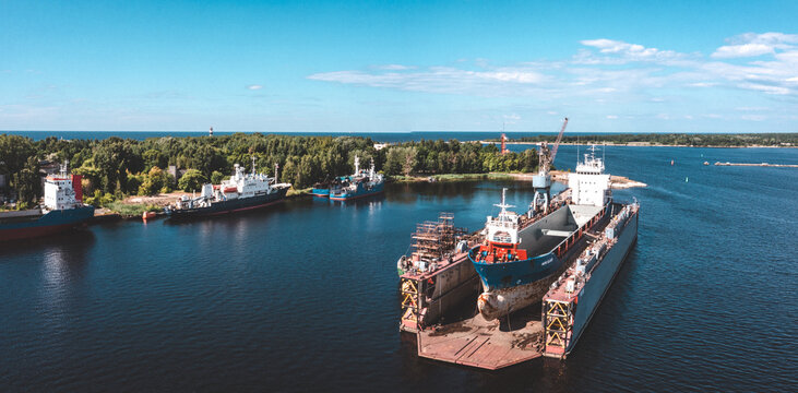 Riga, Latvia. June 10, 2021. Ship in floating dry dock under repair by sandblasting and painting in shipyard. Cargo ship at floating dry dock is being renovated