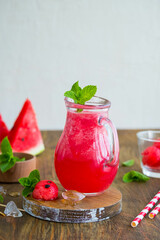 Refreshing soft drink, watermelon lemonade or aqua fresca in a portioned jug on a brown wooden background.