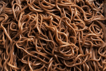 The texture of buckwheat or dark noodles. Brown noodles are visible throughout the frame. An ingredient for making a wok. Asian food. Asian pasta. Cooking food. Strid food. Gluten-free fries. 
