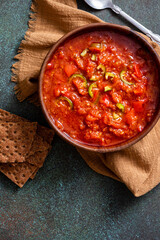 Matbucha - Moroccan Tomato dip. Sauce of tomato, pepper, garlic and chili pepper in a bowl on a dark background top view. Vegan food.