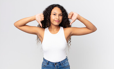 pretty hispanic woman looking sad, disappointed or angry, showing thumbs down in disagreement,...