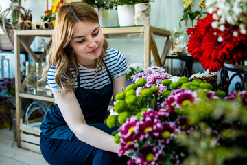 Young adult woman working in city street flower shop.She arranging flowers inside of shop.Small business concept.