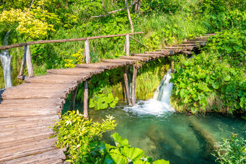 Wooden footpath at Plitvice national park, Croatia. Pathway in the forest near the lake and waterfall. Fresh beautiful nature, peaceful place. Famous tourist destination.