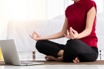 Fototapeta na wymiar Portrait of healthy young Asian woman practicing yoga exercises sitting in the bedroom and learning online on laptop at home. Concept of exercise and relaxation, Technology for New normal lifestyle
