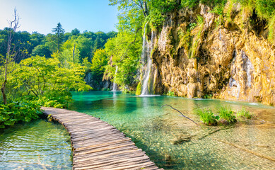 Fototapeta premium Wooden footpath at Plitvice national park, Croatia. Pathway in the forest near the lake and waterfall. Fresh beautiful nature, peaceful place. Famous tourist destination.