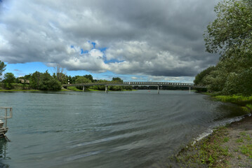 A wooden bridge between the islands of Boucherville national park across St. Lawrence (Laurent) River, Montreal, QC on a cloudy summer day. The trees and grass on the river banks.