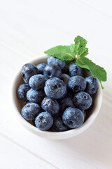 Close-up juicy and fresh blueberries with green mint leaves on white wooden table. Soft focus