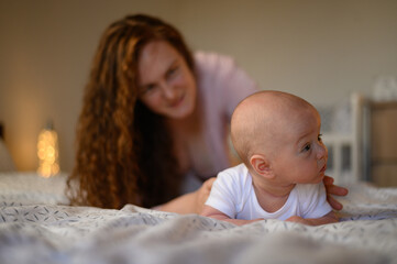 Adorable baby lying on a tummy on the bed while playing with his mother