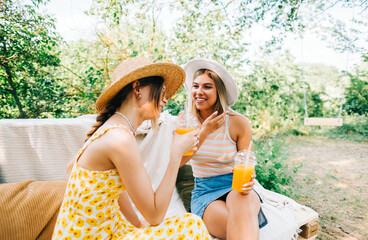 Friends sitting on a sofa in the backyard and drinking orange lemonade on summer sunny day. 