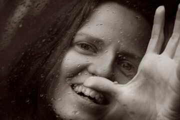 Monochrome portrait of young woman through raindrops on glass