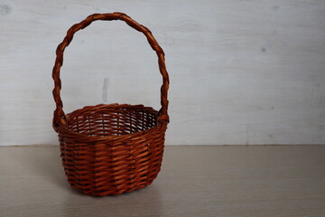 A wicker brown basket stands on a light wooden surface.