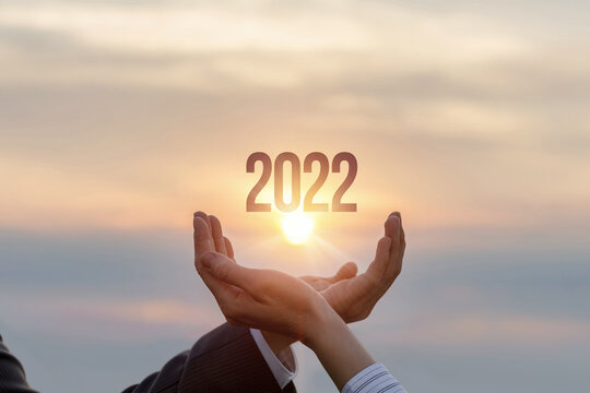 Hands of businessmen show 2022 against the background of a sunny sunset.