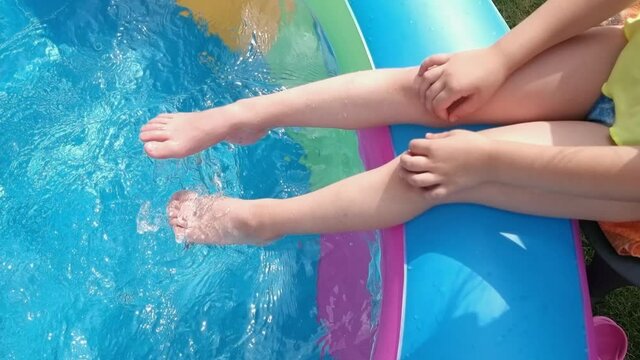 Little girl sits on the edge of the pool and dangles her legs in the water