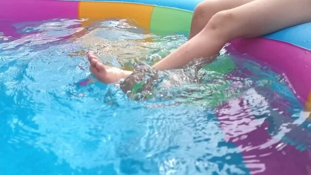 Little girl sits on the edge of the pool and dangles her legs in the water