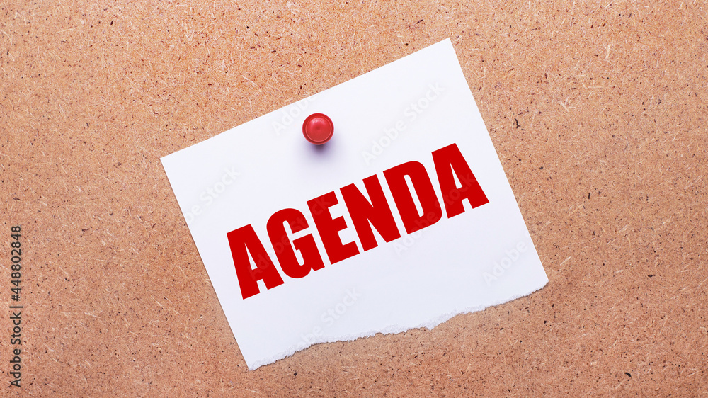 Poster white paper with the text agenda is attached to the wooden background with a red button.