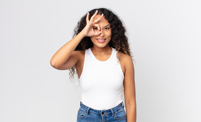 pretty hispanic woman smiling happily with funny face, joking and looking through peephole, spying...