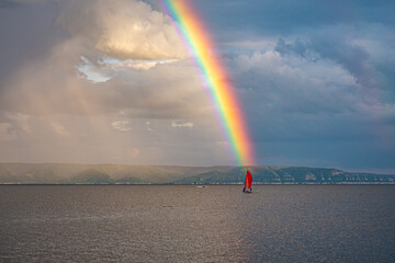 A bright rainbow over the river with a scarlet sail on the horizon