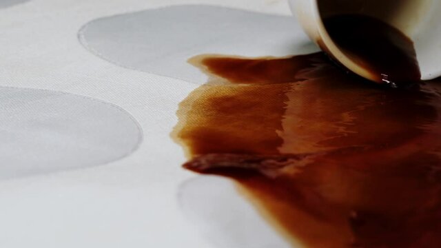 Pouring out coffee on white cloth close-up. Spoiled linen, spilling drink on clothes slow motion shot. 