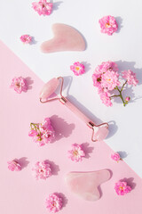 Facial massage kit for home spa. Face roller  and gua sha massager made from rose quartz on white and pink pastel background with rose buds. Natural treatment concept.