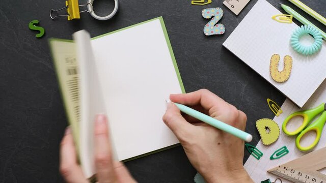 Back to school concept. Person open empty notebook with school supplies on the black background. Top view with copy space. Working table for creative job, study or planning
