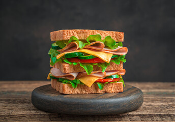 Club sandwich with ham, cheese, vegetables and salad on a brown background. Side view.