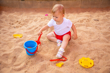 Adorable toddler girl playing with sand on sandbox in playground