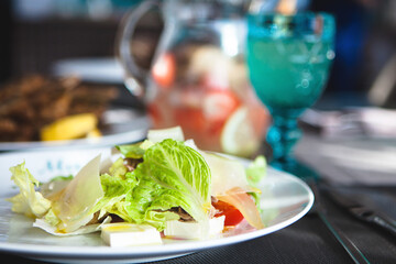 Healthy eating scene. Close up of gourmet delicious salad with fresh lettuce, cherry tomatoes and cheese on a white plate. Front view, selective focus.