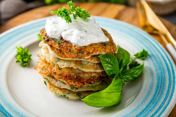 Zucchini pancakes with herbs and sour cream on a blue plate close-up. Vegetarian dish