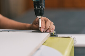 Detail of a man's hand holding a screw and a drill in a workshop