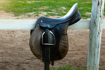 Leather horse saddle on wooden fence.