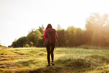 Back view of woman walking with backpack on meadow