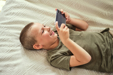 Young boy lying on the bed and playing smartphone. Internet communication, modern technologies and people concept.