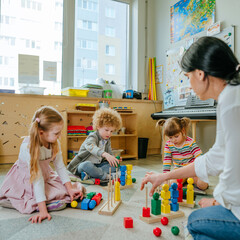 Preschool students sorting wooden geometric shapes sittings on the floor