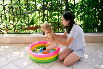 Mom seats little girl in the inflatable pool on the balcony