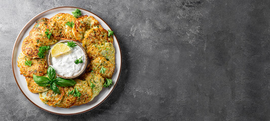 Zucchini pancakes with herbs and sour cream on a plate and gray background top view, web banner with copy space for text. Vegetarian dish