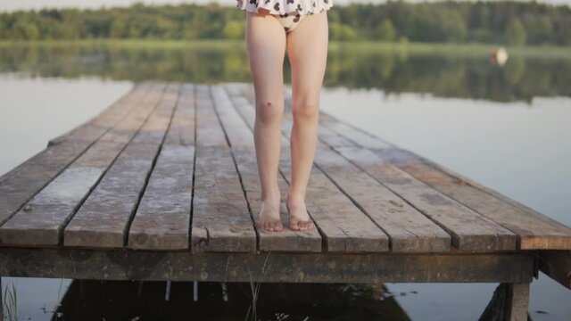 The legs of a little girl on a wooden bridge by the lake in the summer.