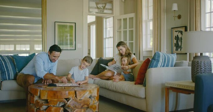 Happy young diverse family relaxing at home in the living room playing board games and reading book, family lifestyle
