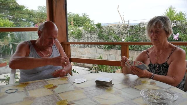 elderly retired couple, husband and wife, play rummy in the summer, under a gazebo in the garden.