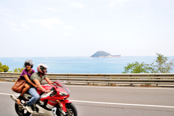 Obraz premium A road along the seashore. Paved road. A man and a woman are riding on a motorcycle. The road along the sea from Italy to France. Cote d'Azur.