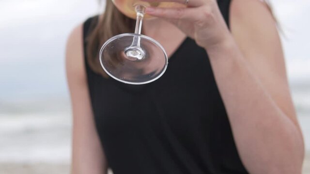 Close-up, slow-motion filming, a woman drinking wine from a glass on the beach by the sea.