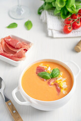 Salmorejo spanish refreshing cold soup usually served in summer made of blended tomatoes and bread decorated with basil leaves, chopped boiled egg and jamon or ham in bowl with spoon and glass of wine