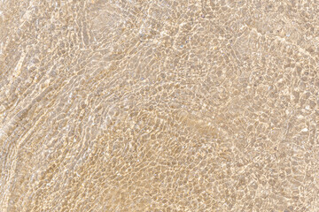 Waves of clear clear water over fine sand, shine and glare. Trending background for different design purposes with copy space. Calm scene, harmony of nature, warm summer day at the sea coast.