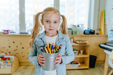 Girl holding color pencils in the kindergarten