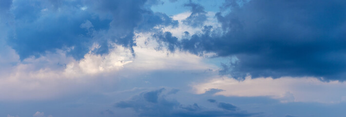 Large dark clouds obscure small light clouds in the evening sky, panorama