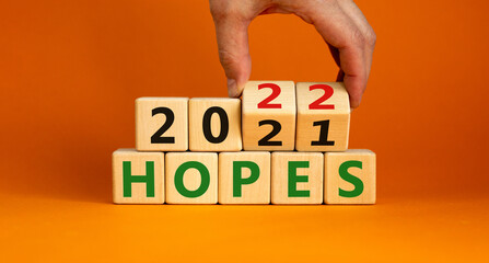 2022 hopes new year symbol. Businessman turns wooden cubes and changes words 'Hopes 2021' to 'Hopes 2022'. Beautiful orange background, copy space. Business, 2022 hopes new year concept.