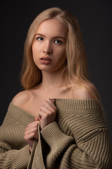 Portrait of a young attractive girl with long curly hair in a warm jacket. The blonde. Black background.