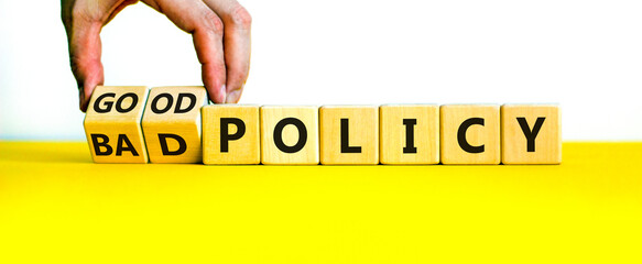 Good or bad policy symbol. Businessman turns wooden cubes and changes words 'bad policy' to 'good policy'. Beautiful yellow table, white background. Business, bad or good policy concept. Copy space.