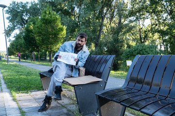 Young sick helpless desperate homeless man sitting on the bench on the urban street in the city...